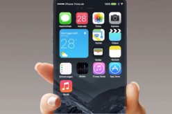 A smartphone, bearing iPhone logos, is held by a hand to showcase its edge to edge display.