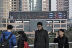 Pedestrians walk past a large screen showing financial data in Shanghai, on Jan. 4, 2017.