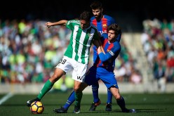Real Betis striker Alex Alegria (L) competes for the ball against two Barcelona players.
