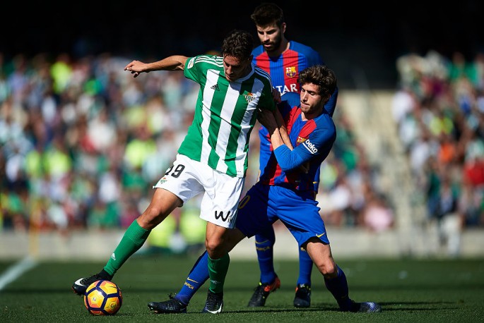 Real Betis striker Alex Alegria (L) competes for the ball against two Barcelona players.
