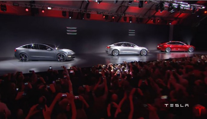 Tesla Model 3 cars are showcased in front a massive crowd.