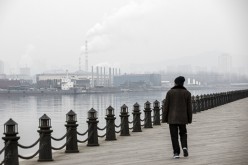 A man strolls along a waterfront boardwalk facing factories and a shipbuilding yard in Dalian, China.