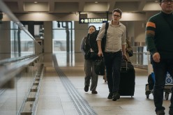Travelers carrying luggage walk through an airport.
