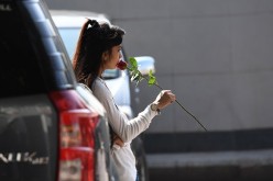 A young woman holds a rose as she waits in a parking area.
