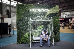 An attendee sits in front of a signage for smartphone maker Oppo at the Mobile World Congress Shanghai in Shanghai, China.
