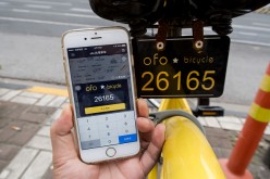 A passenger uses app on the phone to check mileage of a yellow rental bike at the service points of Zhoujiazui Road.