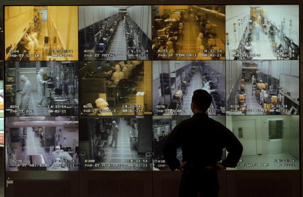 A man observes semiconductor manufacturing on wall of monitors.