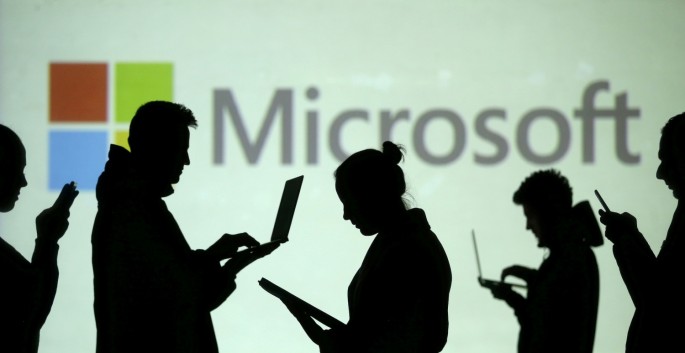 Silhouettes of laptop and mobile device users are seen next to a screen projection of Microsoft logo in this picture illustration taken 