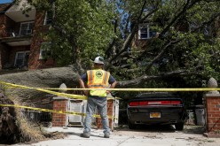 A New York City worker looks at the damage from a tree that has fallen on a house and car during the clean up of Tropical Storm Isaias in the Astoria neighborhood of Queens,