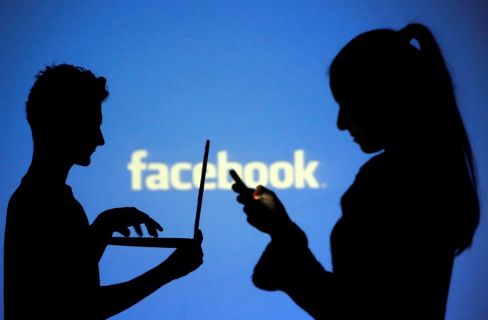 People are silhouetted as they pose with laptops in front of a screen projected with a Facebook logo, in this picture illustration taken in Zenica