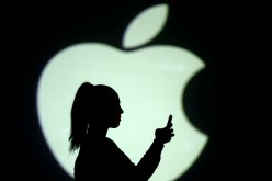 Silhouette of a mobile user seen next to a screen projection of the Apple logo in this picture illustration taken 
