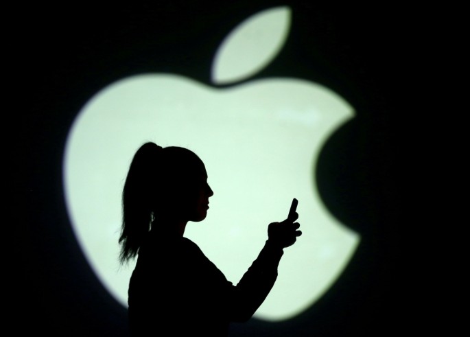 Silhouette of a mobile user seen next to a screen projection of the Apple logo in this picture illustration taken 