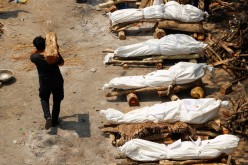 A man carrying wood walks past the funeral pyres of those who died from the coronavirus disease (COVID-19), during a mass cremation, at a crematorium in New Delhi