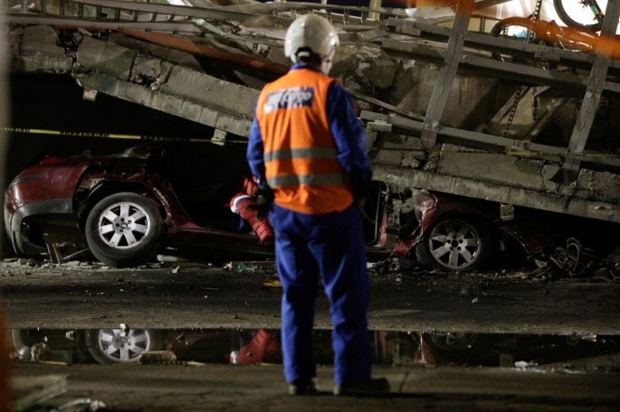 A rescue worker stands in front of a car trapped under an overpass for a metro that partially collapsed with train cars on it at Olivos station in Mexico City