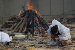 A man mourns as he sits next to the burning pyre of a relative, who died from the coronavirus disease (COVID-19), during his cremation, at a crematorium in New Delhi, India