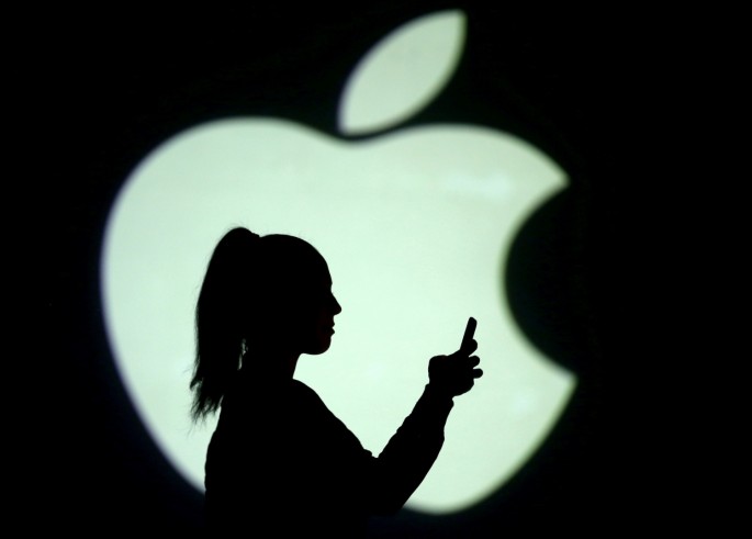 Silhouette of a mobile user seen next to a screen projection of the Apple logo in this picture illustration