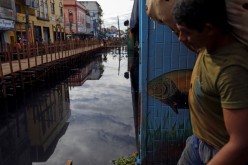 A man carries a bag as he walks over wooden walkways installed by the city hall over a street flooded by waters from the Negro river in downtown of Manaus, in Amazonas State, Brazil