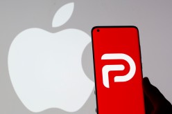Woman holding smartphone with Parler logo in front of displayed Apple logo in this illustration