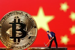 A small toy figurine is seen on representations of the Bitcoin virtual currency displayed in front of an image of China's flag
