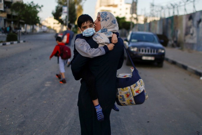A Palestinian woman carrying her son evacuates after their tower building was hit by Israeli air strikes, amid a flare-up of Israeli-Palestinian violence, in Gaza City 