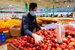 Wearing a mask and gloves, a worker re-stocks apples in an Asian grocery store in Falls Church, Virginia, U.S.