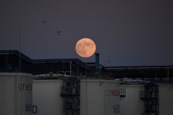 The moon rises behind the storage tanks of a local oil refinery in Omsk, Russia