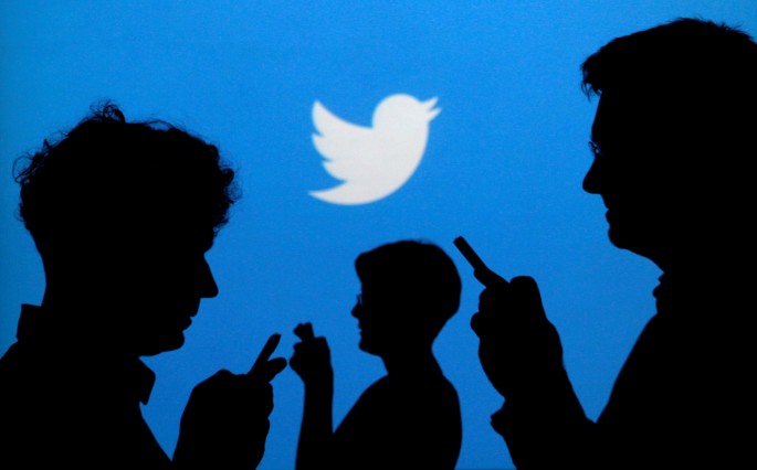 People holding mobile phones are silhouetted against a backdrop projected with the Twitter logo in this illustration picture taken