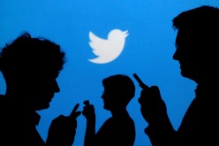 People holding mobile phones are silhouetted against a backdrop projected with the Twitter logo in this illustration picture taken