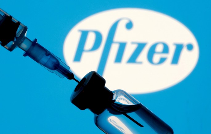 A vial and syringe are seen in front of a displayed Pfizer logo in this illustration taken