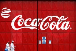 Workers walk past a Coca Cola logo painted on a gate at a Coca Cola factory in Nairobi,