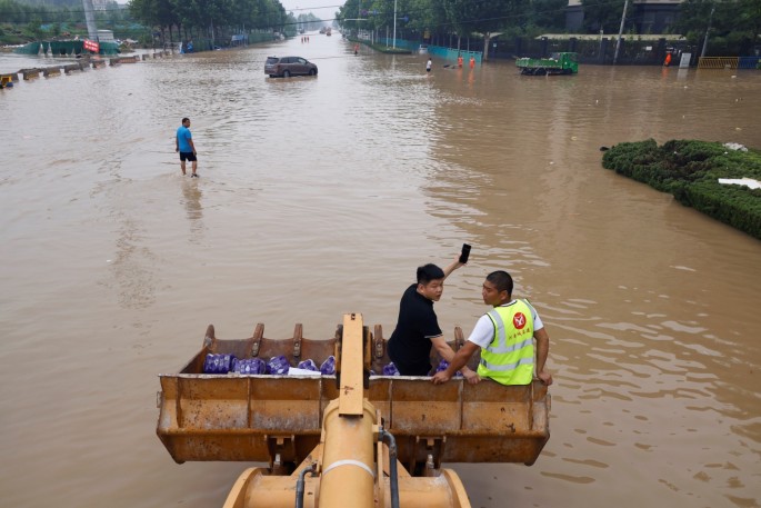 A front loader carries people and water supplies through a flooded road following heavy rainfall in Zhengzhou, Henan province,