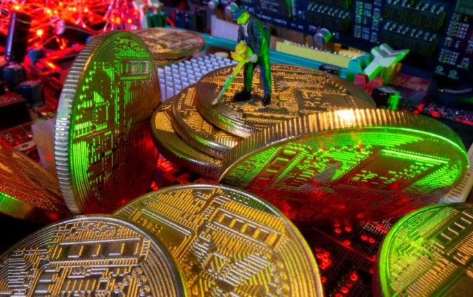 A small toy figure and representations of virtual currency stand on a motherboard in this picture illustration taken