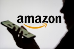 Woman with smartphone is seen in front of displayed Amazon logo in this illustration