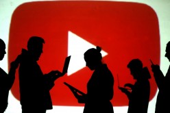 Silhouettes of laptop and mobile device users are seen next to a screen projection of the YouTube logo in this picture illustration taken 