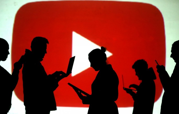 Silhouettes of laptop and mobile device users are seen next to a screen projection of the YouTube logo in this picture illustration taken 