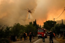 A firefighting helicopter makes a water drop as a wildfire burns in the village of Vilia, Greece,