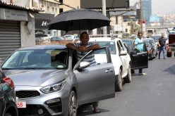 A man shields from the sun with an umbrella as he waits to get fuel from a gas station in Jal el-Dib, Lebanon