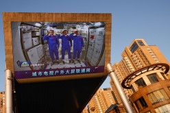 A giant screen shows Chinese astronauts Nie Haisheng (C), Liu Boming (R), and Tang Hongbo of the Shenzhou-12 mission saluting inside the Tianhe core module of China's space station, at a shopping mall in Beijing,