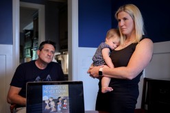 Robin Steenman, chair of the local chapter of Moms for Liberty, holds her 10-month-old daughter Judith, alongside fellow concerned parent Brett Craig, in front of a power point presentation highlighting the types of books Moms 