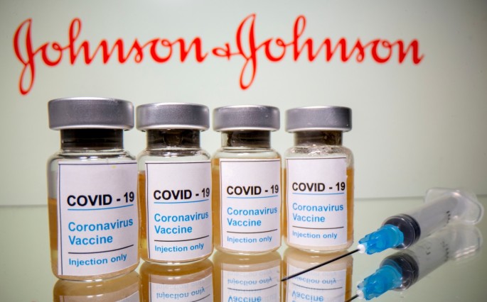Vials with a sticker reading, "COVID-19 / Coronavirus vaccine / Injection only" and a medical syringe are seen in front of a displayed Johnson & Johnson logo