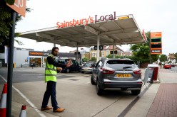 A worker guides vehicles into the forecourt as they queue to refill at a fuel station in London,