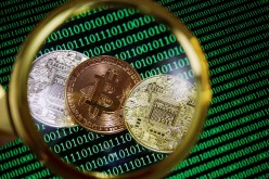 Representations of Bitcoin and other cryptocurrencies on a screen showing binary codes are seen through a magnifying glass in this illustration picture taken 