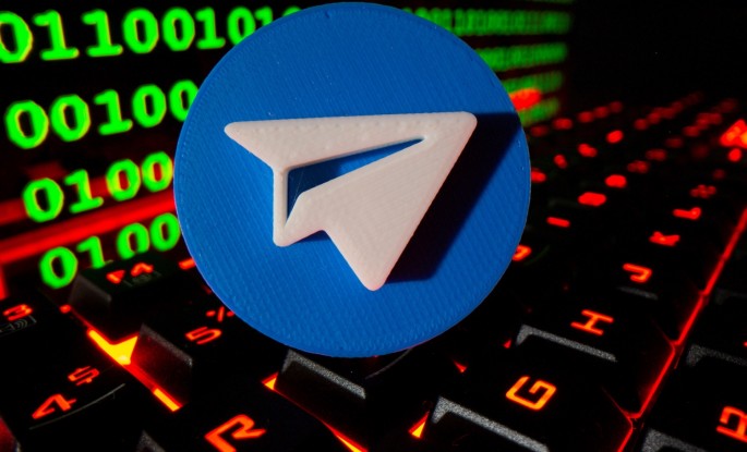 A 3D printed Telegram logo is pictured on a keyboard in front of binary code in this illustration taken
