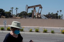 A pedestrian wearing a protective mask walks past an oil derrick in Huntington Beach during the outbreak of the coronavirus disease (COVID-19) in Huntington Beach, California, U.S.,