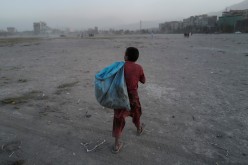 Eftekhar, 14, carries a bag filled with plastic bottles he collected, to be sold, as he walks in a playground in Kabul, Afghanistan