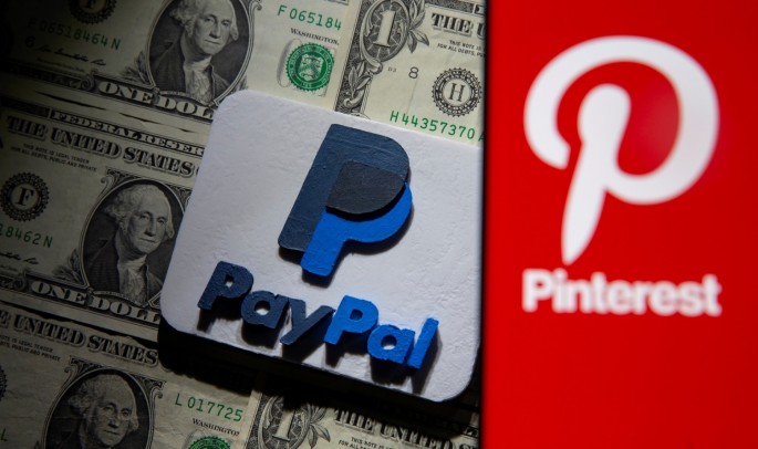 A Pinterest logo is seen on a smartphone placed over U.S. dollar banknotes and a 3D printed PayPal logo in this illustration taken