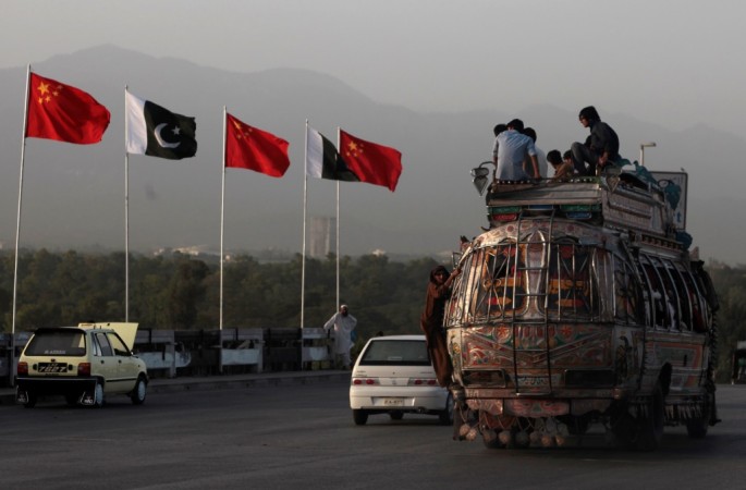 People sit on top of a bus as they go past flags of Pakistan and China displayed along a road in Islamabad. 