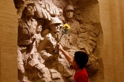 A boy places a flower on a sculpture depicting Chinese fighters during the World War II. 