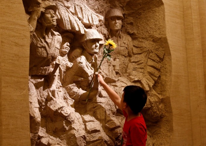 A boy places a flower on a sculpture depicting Chinese fighters during the World War II. 