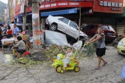 A woman pushes a baby on bike next to damaged cars and debris in Beijing. 